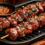 Chinese lamb skewers grilled over charcoal, served on a wooden board with spices and dipping sauce.