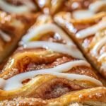 Golden-baked cinnamon-sugar pizza made with crescent rolls, sliced into squares and drizzled with icing on a wooden board