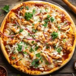 Freshly baked BBQ chicken pizza with melty cheese, red onions, and cilantro on a rustic wooden table.